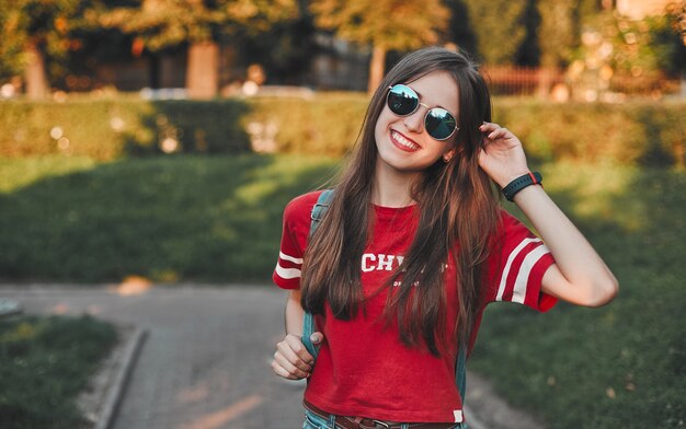 Um estudante com uma camiseta vermelha e uma mochila com óculos de sol na rua