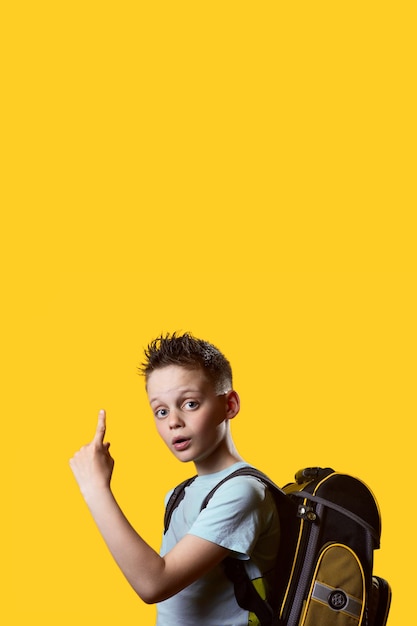 Um estudante do primeiro ano de volta à escola em setembro com uma mochila e livros didáticos em um conceito de outono de fundo amarelo