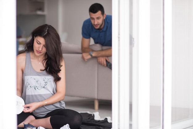 um feliz casal grávido verificando uma lista de coisas para seu bebê por nascer em casa no chão