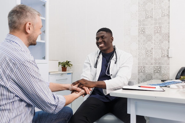 Um feliz e sorridente médico afro-americano apoia o paciente durante a sessão de consulta