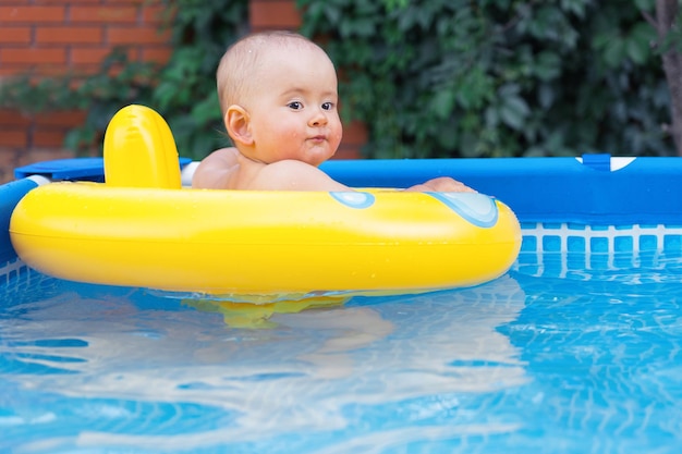 Um feliz recém-nascido de 10-12 meses está nadando em um ringue de natação. Piscina de armação no quintal da casa