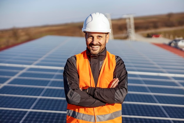 Um feliz trabalhador orgulhoso de pé no telhado com painéis solares e apoiando a vida ecológica