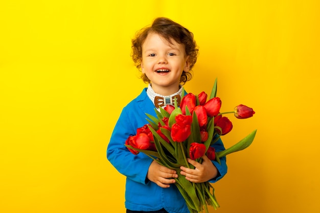 Um filho feliz, um menino com uma jaqueta azul e uma borboleta segura um enorme buquê de tulipas vermelhas