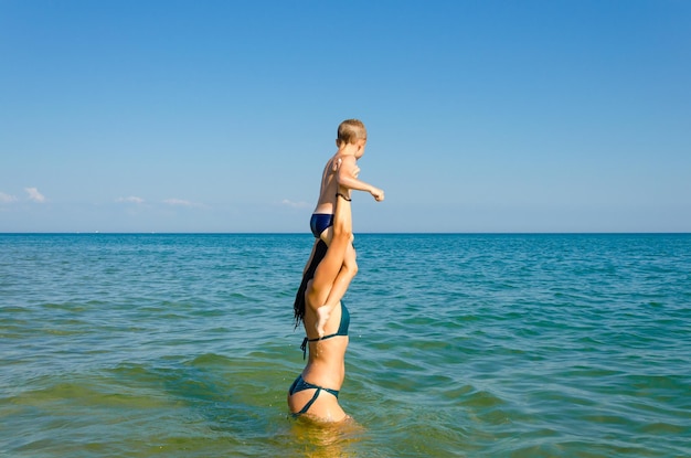 Um filho pequeno com sua mãe nada no mar no verão.