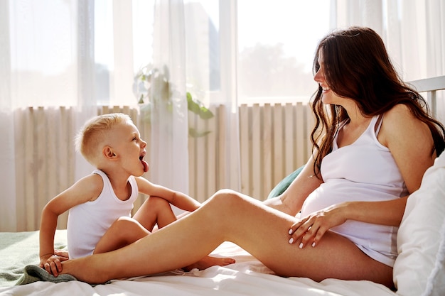 Foto um filho pequeno e sua mãe grávida estão deitados na cama.