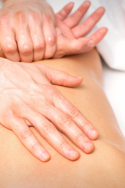 Foto um fisioterapeuta estende os braços nas costas de um homem deitado, de perto.