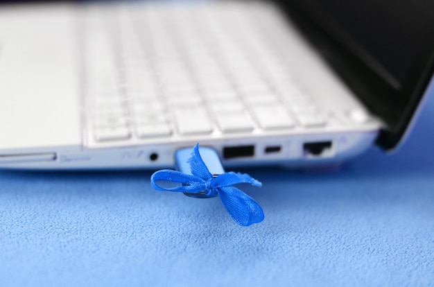 Um flash drive USB azul brilhante com um laço azul está conectado a um laptop branco