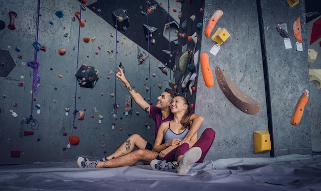 Um forte casal de alpinistas contra uma parede artificial com cabos e cordas coloridas