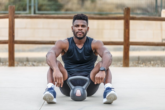 Um forte desportista preto a descansar perto do kettlebell.