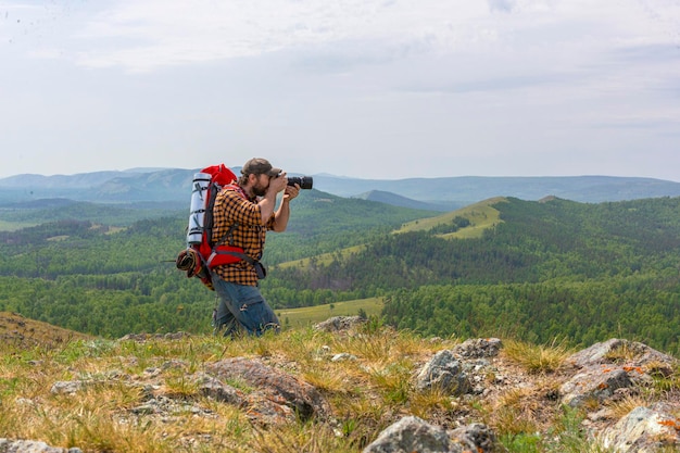 Um fotógrafo com uma mochila grande tira uma foto nas montanhas