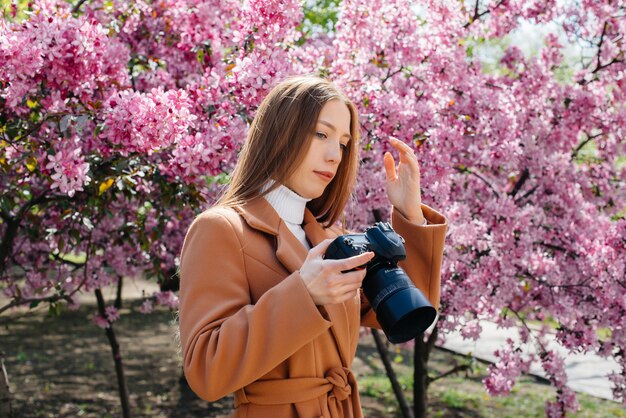 Um fotógrafo jovem bonita caminha e tira fotos contra uma macieira florescendo.