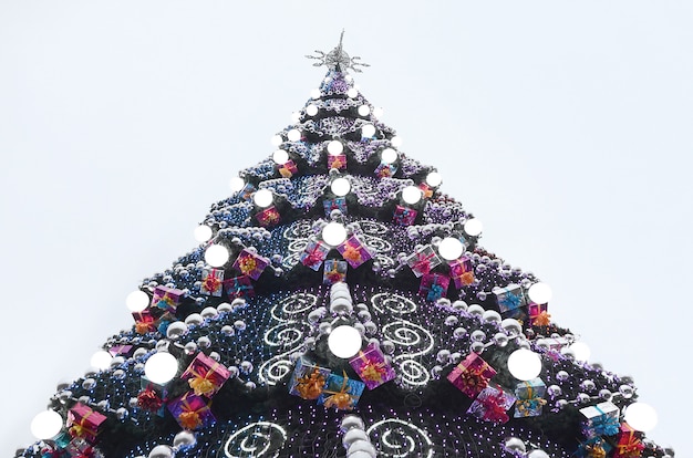 Um fragmento de uma enorme árvore de Natal com muitos ornamentos, caixas de presente e lâmpadas luminosas