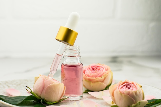 Um frasco aberto de óleo de rosa e uma pipeta cheia de cosméticos para rejuvenescimento e cuidados com a pele facial em um prato de cerâmica.