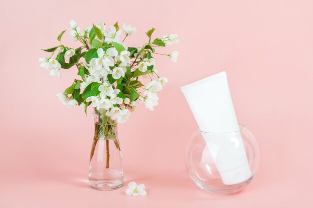 Um frasco cosmético branco em branco e um ramo florido em um vaso