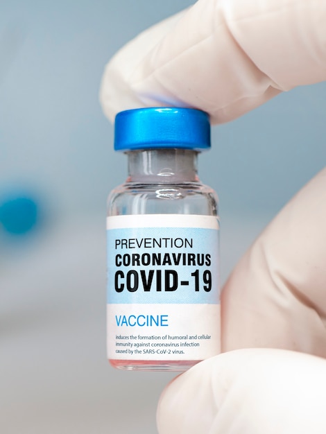 Um frasco de close-up de vacina na mão de um médico com luvas brancas sobre fundo azul.