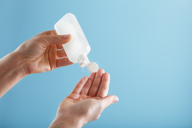 Um frasco de gel desinfetante em suas mãos, sobre um fundo azul. Tratamento anti-séptico das mãos das bactérias Sanitizer.