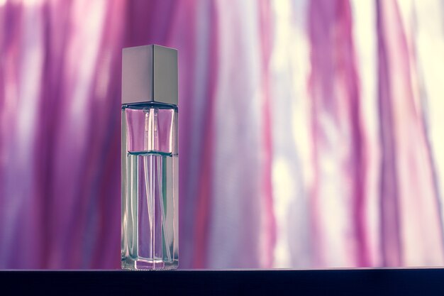 Um frasco de perfume alongado facetado fica sobre um fundo rosa claro desfocado. Frasco de vidro com tampa de metal. Em branco para simulação. Foco seletivo. Horizontal.