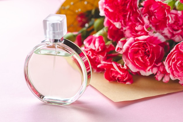 Um frasco de perfume de pessoa e um buquê de flores em um surfce rosa. Dê presentes e flores para a pessoa. Receba presentes de pessoas queridas nos feriados