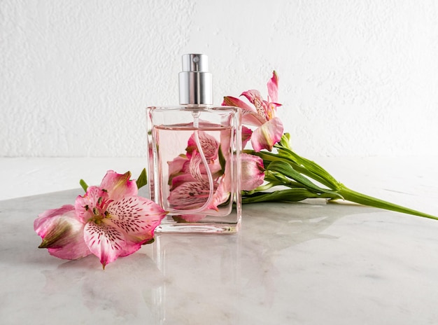 Um frasco de perfume em uma laje de mármore contra o fundo de uma parede texturizada e um conceito de publicidade de flor rosa da perfumaria feminina