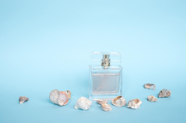 Um frasco de perfume fica em um fundo azul perto de conchas