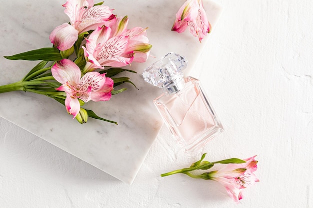 Um frasco de perfume ou água de toalete com um leve aroma floral apoiado em uma laje de mármore branco com apresentação de aroma de fundo branco de flores rosa