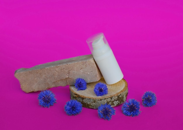 Um frasco de plástico branco para cosméticos fica em um pódio de madeira com flores azuis em um fundo rosa