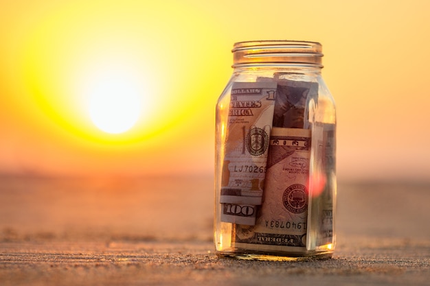 Um frasco de vidro com moedas e notas na praia. o conceito de acúmulo de dinheiro para viagens.