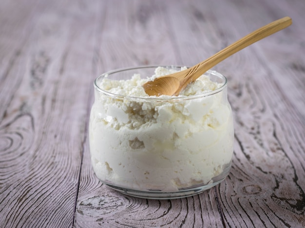 Um frasco de vidro com queijo fresco e uma colher de pau em uma mesa de madeira rosa. O conceito de alimentação saudável.