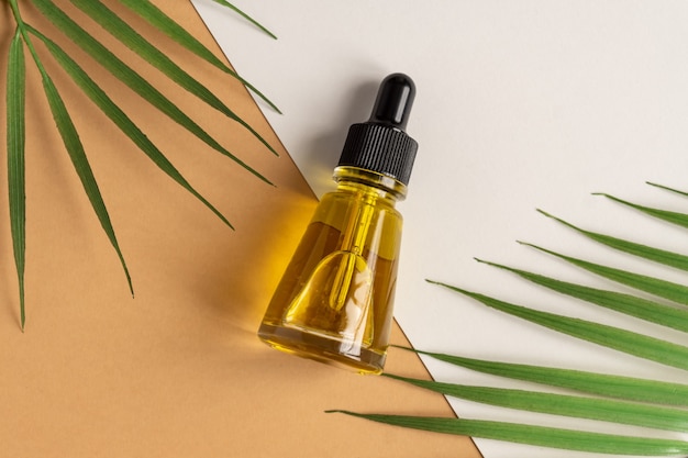 Um frasco de vidro cosmético com um conta-gotas em uma parede bege com folhas tropicais. Conceito de cosméticos naturais, óleo essencial natural.