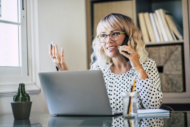 Um freelance adulto jovem feliz no trabalho no escritório doméstico Mulher profissional com laptop usando telefone para ligar para clientes remotos Ajudar assistência on-line Pessoas e atividade de estilo de vida de conceito de trabalho inteligente