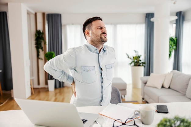 Um freelancer com dor nas costas por sentar e trabalhar em casa