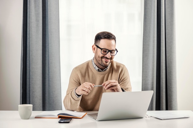 Um freelancer feliz sentado em seu escritório em casa trabalhando e olhando para o laptop
