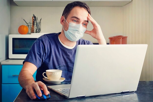 Foto um funcionário cansado trabalha em um escritório doméstico. jovem usando máscara médica no trabalho do escritório em casa devido ao surto do vírus corona com o laptop na mesa. trabalho remoto.