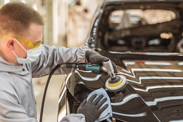 um funcionário da oficina de luvas e máscara dá brilho à superfície pintada da fábrica de automóveis