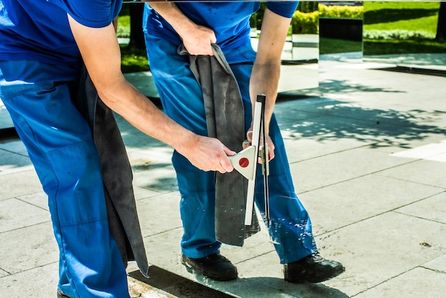 Um funcionário de uma empresa de limpeza lava um espelho raspador de vidro limpando o parque em um dia de verão mãos masculinas