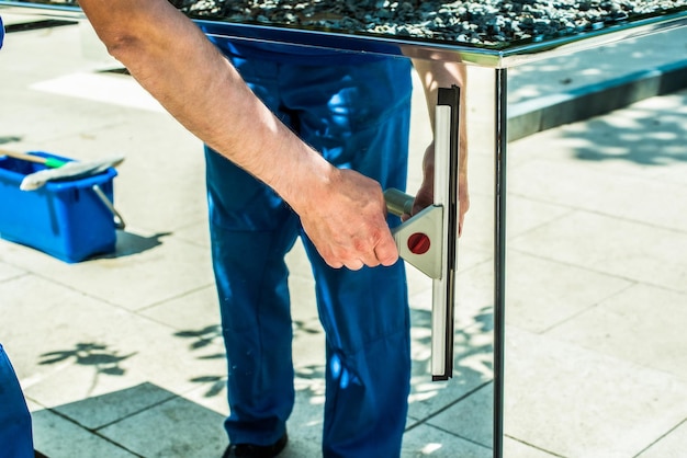 Um funcionário de uma empresa de limpeza lava um espelho raspador de vidro limpando o parque em um dia de verão mãos masculinas