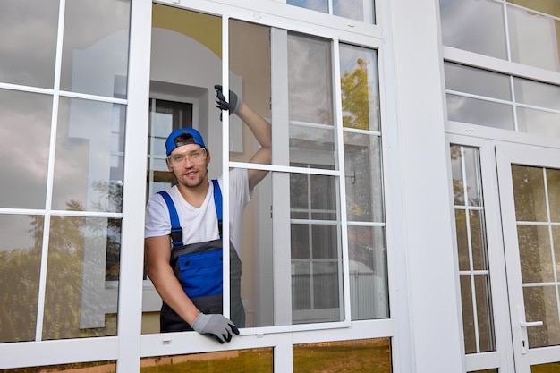 Um funcionário experiente de uma empresa de vitrines posa realizando o trabalho de instalação de uma rede mosquiteira Profissional bonito sorrindo olha para a câmera e segura uma rede de insetos