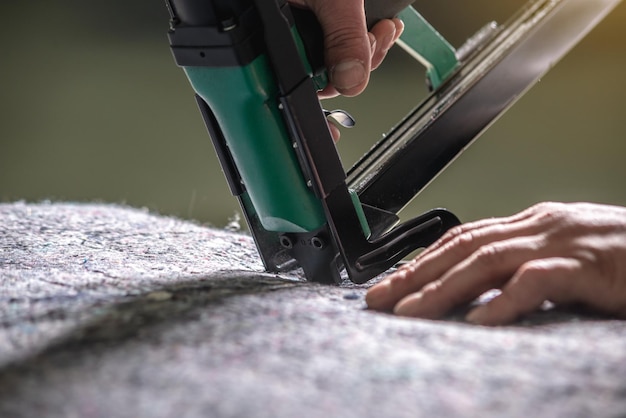 Um funcionário segura em suas mãos um grampeador de ar industrial para embainhar estofamento de tecido macio closeup