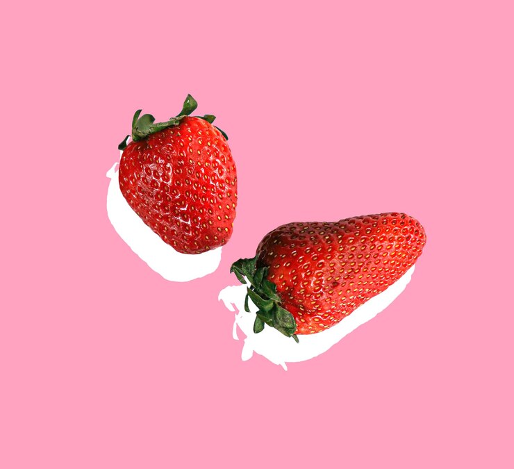 Foto um fundo rosa com dois morangos e um com creme branco.