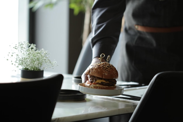 Um garçom colocando um prato de sanduíche de hambúrguer em uma mesa branca em um restaurante