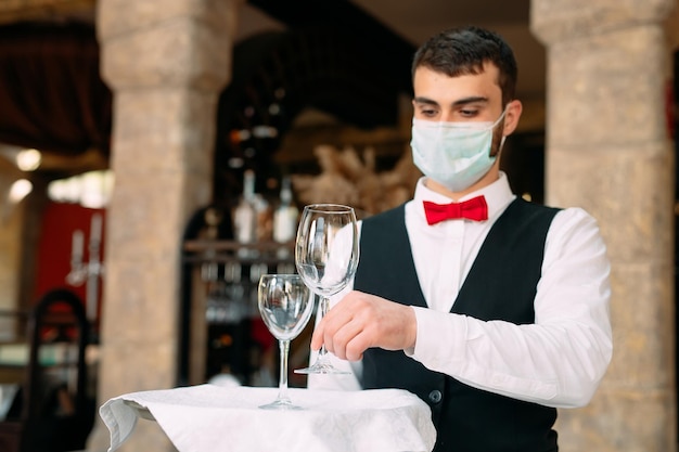 Um garçom com uma máscara de proteção médica serve a mesa no restaurante.