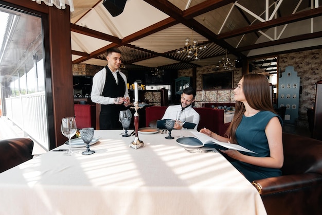 Um garçom elegante serve um jovem casal de um homem e uma mulher que veio a um restaurante gourmet Atendimento ao cliente no restaurante e estabelecimentos de catering