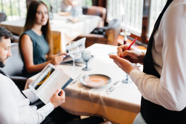 Um garçom estiloso serve um jovem casal que saiu para um encontro em um restaurante gourmet. atendimento ao cliente na área de catering.