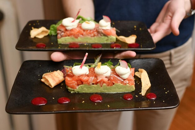 Um garçom segurando pratos de salmão e guacamole