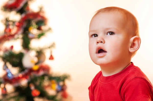 Um garotinho à espera de presentes do papai noel está triste e chorando perto da árvore do ano novo.