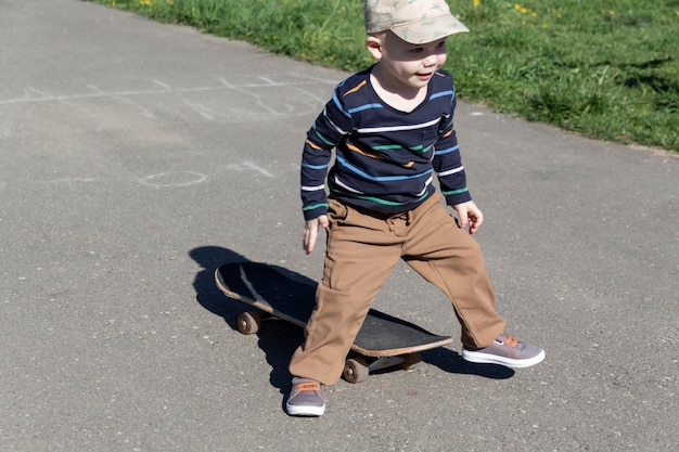 Um garotinho aprende esportes radicais de skate no verão no playground no parque e ao ar livre