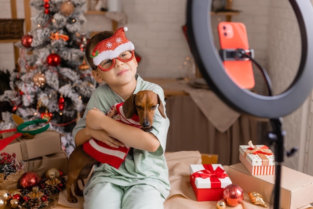 Um garotinho blogueiro com um dachshund de cachorro de estimação grava um blog em casa na cozinha em