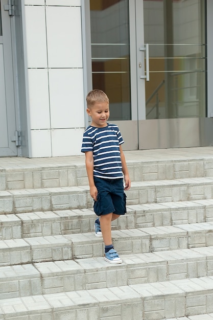 Um garotinho caminha sozinho, sai do prédio e desce a escada