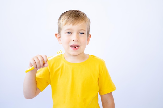 Um garotinho com cabelos loiros e olhos azuis, uma criança em um fundo branco está escovando os dentes, segurando uma escova de dentes nas mãos isolada