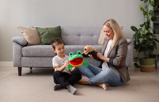 Um garotinho com sua mãe está sentado no tapete perto do sofá e jogando teatro de fantoches com um macaco e um sapo